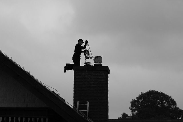 Silhouette of a chimney sweep coiling line atop a stack at dusk